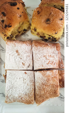 Warm pastries scattered on delicate paper doily, featuring chocolate studded treats and sugar dusted delights beckoning sweet toothed food lovers 123204881