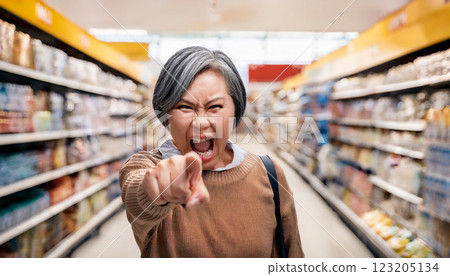 A woman is furious and pointing at someone in a supermarket. Customer harassment. 123205134