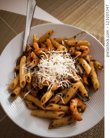 Penne pasta garnished with dill, topped with succulent shrimp and parmesan, resting on white ceramic plate in prague dining setting Galentines day Penne pasta garnished with dill, topped with succulent shrimp and parmesan, resting on white ceramic plate in prague dining setting Galentines day 123205347