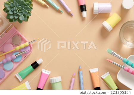 Frame with art supplies in green, yellow, pink and purple pastel colors on a beige background. Paints, colored pencils and brushes. Space for your text. 123205394