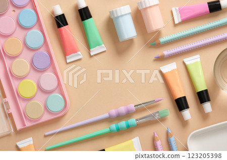 Frame with art supplies in green, yellow, pink and purple pastel colors on a beige background. Paints, colored pencils and brushes. Space for your text. 123205398
