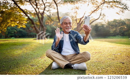 A senior man making a video call on his smartphone in the park. 123206539