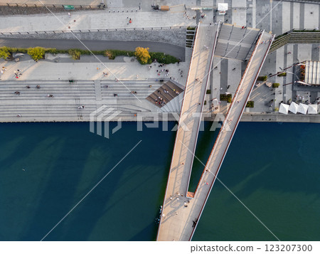 pedestrian bridge over blue Vistula river, people walking at shore and embankment, Warsaw, aerial top view 123207300