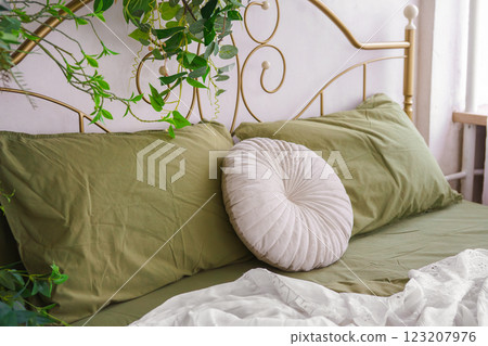 Round white plush decorative pillow on bed with green bedding, home decor, bedroom interior 123207976