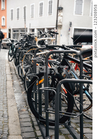 Row of urban bicycles parked in a metal bike rack along a cobblestone street. The European cityscape 123208958