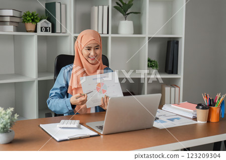 Muslim woman in hijab presenting a report with a pie chart during a video call in a modern office. 123209304