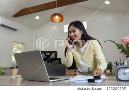 Businesswoman on the phone while working on laptop and reviewing documents at home Businesswoman on the phone while working on laptop and reviewing documents at home 123209305
