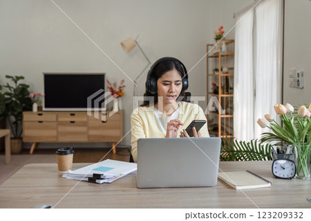 Focused woman working from home with laptop and smartphone, managing tasks and responsibilities. 123209332