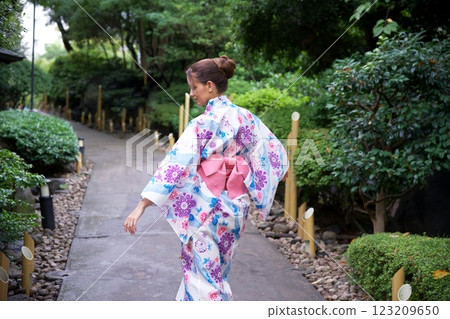 Woman in Floral Kimono Gracefully Walking Through Garden  123209650