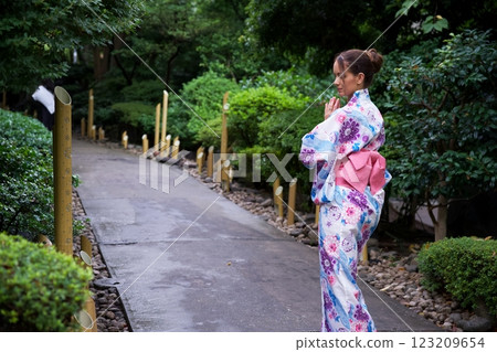 Woman in Floral Kimono Meditating on Garden Pathway  123209654
