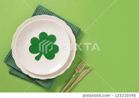 St Patrick's Day table setting with white plate and traditional decoration with shamrock on green background. View from above. Copy space. 123210348