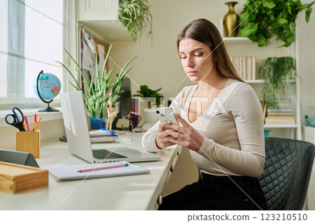 Serious young woman using smartphone, sitting at home 123210510