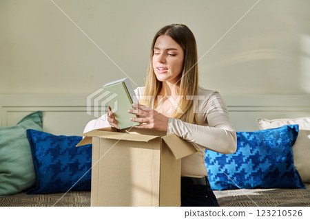 Young woman unpacking cardboard with online order, looking at new cosmetics perfumes 123210526