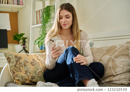 Young smiling woman looking at smartphone sitting on couch at home 123210539