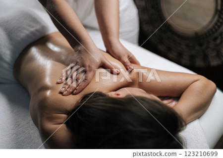 Closeup of massage therapist rubbing moisturizing oil into client shoulder and back during therapeutic treatment at serene wellness spa, targeting muscle tension and promoting relaxation Closeup of massage therapist rubbing moisturizing oil into client shoulder and back during therapeutic treatment at serene wellness spa, targeting muscle tension and promoting relaxation 123210699