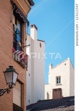 Bright balcony adorned with flowers is situated on a historic brick building, contrasting with nearby white structures under a clear blue sky in a lively urban setting. 123211547