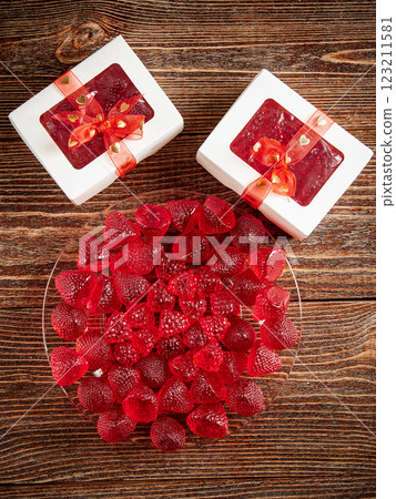 Sweets in the shape of strawberries and raspberries in festive packages. Wooden brown background. Sweets in the shape of strawberries and raspberries in festive packages. Wooden brown background. 123211581