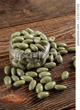Green chocolates on a brown wooden background. Sweets in a glass jar. Green chocolates on a brown wooden background. Sweets in a glass jar. 123211582