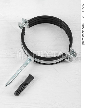 Clamp with a rubber gasket and fasteners on a white wooden background. Pipe holder, protection against water leaks. 123211597