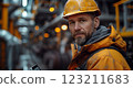 An engineer in workwear and headgear holds a cell phone in a factory setting 123211683