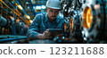 An engineer in electric blue workwear is using a tablet in a factory 123211688