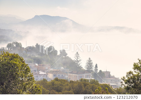 Malaga, seaside city in Andalusia, Spain, Europe. Misty mountain village, serene landscape. Houses nestled in hills, shrouded in fog. Tranquil scene. Malaga, seaside city in Andalusia, Spain, Europe. Misty mountain village, serene landscape. Houses nestled in hills, shrouded in fog. Tranquil scene. 123212070
