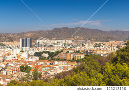Malaga, seaside city in Andalusia, Spain, Europe. Panoramic view of a city nestled against mountains under a clear blue sky. Buildings, trees, and hills create a picturesque landscape. 123212138