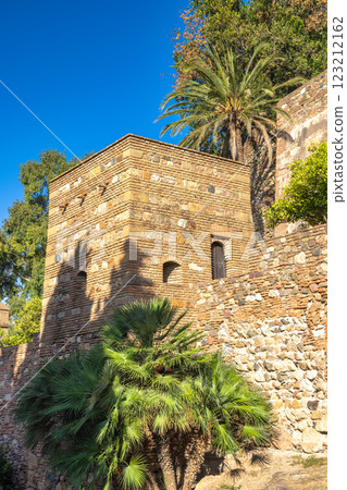 Alcazaba, palace and fortification in Malaga city at Andalusia, Spain, Europe. Ancient stone tower and wall, bathed in sunlight, with lush palm trees adding to the scene's serenity. Alcazaba, palace and fortification in Malaga city at Andalusia, Spain, Europe. Ancient stone tower and wall, bathed in sunlight, with lush palm trees adding to the scene's serenity. 123212162