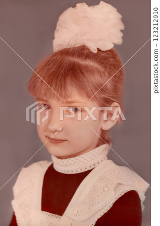 First-grader girl, seven years old, with a bow on her head and in a school uniform, apron. Vintage photo from 1988. USSR 123212910
