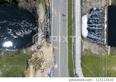 Damaged road bridge destroyed by river after flood water washed away asphalt. Rebuilding of ruined transportation infrastructure 123213810