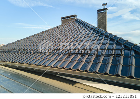 Closeup snow guard for safety in winter on house roof top covered with ceramic shingles. Tiled covering of building Closeup snow guard for safety in winter on house roof top covered with ceramic shingles. Tiled covering of building 123213851