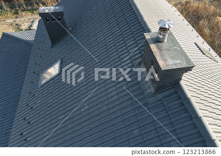 Closeup of attic windows and brick chimneys on house roof top covered with ceramic shingles. Tiled covering of building 123213866