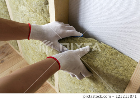 Close-up of worker hands in white gloves insulating rock wool insulation staff in wooden frame for future walls for cold barrier. Comfortable warm home, economy, construction and renovation concept. 123213871