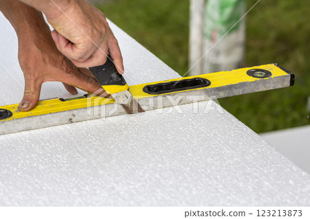 Close-up of worker hand with knife and level cutting white rigid polyurethane foam sheet for house insulation. Modern technology, renovation, professional job, alternative for mineral wool concept. Close-up of worker hand with knife and level cutting white rigid polyurethane foam sheet for house insulation. Modern technology, renovation, professional job, alternative for mineral wool concept. 123213873