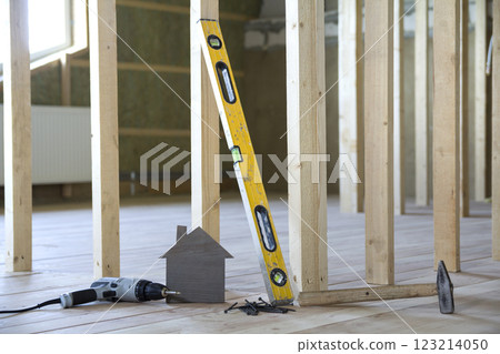 Close-up of small brown model house and building tools on wooden planks in unfinished room under construction background. Investments in real estate, property and ownership of dream home concept. 123214050