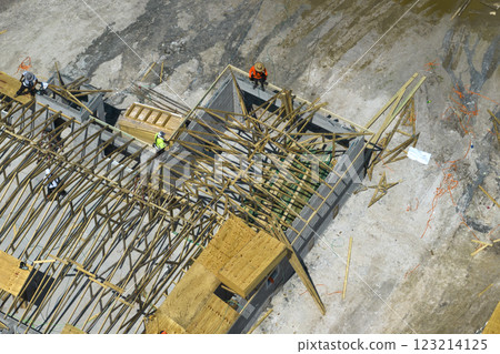 Builders working on roof construction of unfinished residential house with wooden frame structure in Florida suburban area. Housing development concept 123214125