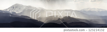 Breathtaking panoramic view of magnificent foggy Carpathian mountains, covered with ever-green forest on misty quiet morning or evening under dark cloudy sky. Mountains snow covered tops in distance. 123214132