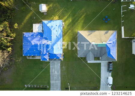 Aerial view of damaged in hurricane Ian houses roofs covered with blue protective tarp against rain water leaking until replacement of asphalt shingles Aerial view of damaged in hurricane Ian houses roofs covered with blue protective tarp against rain water leaking until replacement of asphalt shingles 123214625