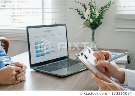 Professionals discussing trending products with a laptop and clipboard in a modern office environment. Professionals discussing trending products with a laptop and clipboard in a modern office environment. 123215084