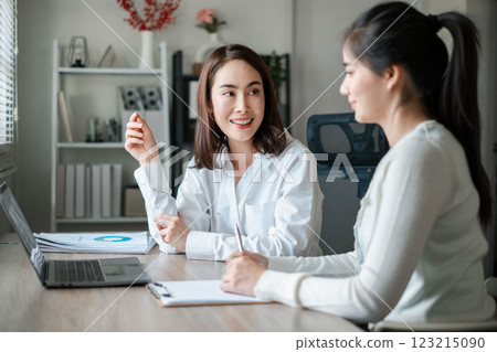 Two women discussing business strategies in a modern office setting, showcasing teamwork and collaboration. 123215090