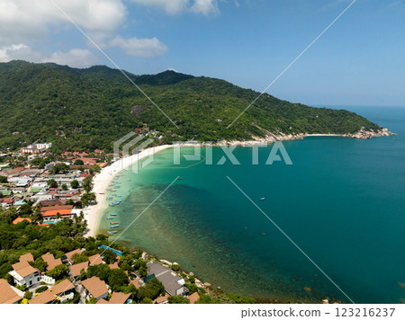 Turquoise bay lined with a white sandy beach and surrounded by lush green hills under a sunny sky. Haad Rin. Ko Pha Ngan, Thailand. 123216237