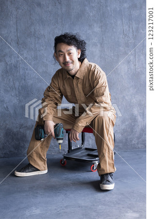 一名穿著工作服和工作服的建築工人拿著工具坐在椅子上 123217001