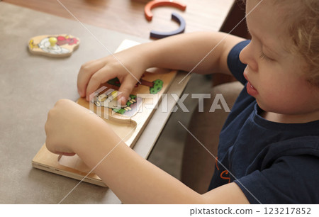 Little boy plays with educational game on table. Wooden puzzle. Animals and farm.  123217852