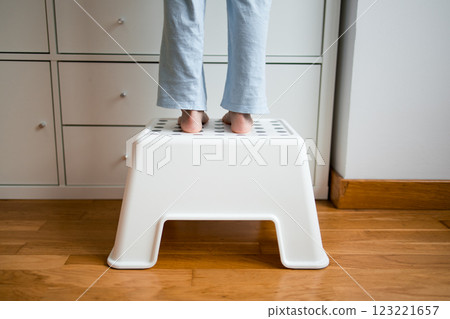 Child standing on white step stool reaching high shelf in home setting Child standing on white step stool reaching high shelf in home setting 123221657