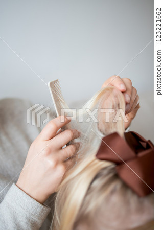 Female caucasian young adult combing blonde hair with brown bow in neutral background Female caucasian young adult combing blonde hair with brown bow in neutral background 123221662