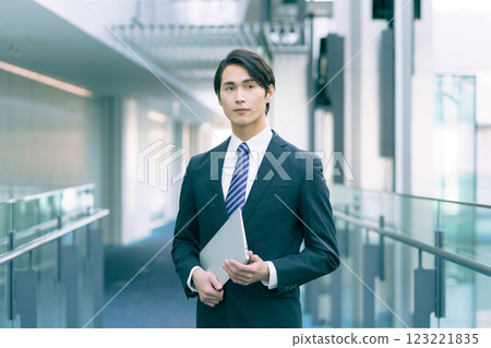 A young businessman wearing a suit and holding a PC standing in an aisle. Photo courtesy of Sky Perfect Tokyo Media Center 123221835