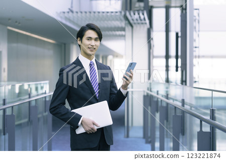 一位身穿西裝、手拿電腦、操作智慧型手機的年輕商人。 一位身穿西裝、手拿電腦、操作智慧型手機的年輕商人。 123221874