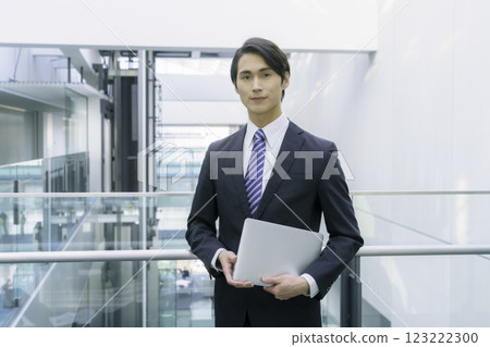 A young businessman wearing a suit and holding a PC standing in an aisle. Photo courtesy of Sky Perfect Tokyo Media Center 123222300