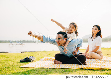Asian family sitting playing on picnic blanket spring meadow field grass in park, Happy parents child girl riding father back enjoying outdoors together, father carrying daughter, Family relaxation Asian family sitting playing on picnic blanket spring meadow field grass in park, Happy parents child girl riding father back enjoying outdoors together, father carrying daughter, Family relaxation 123222726