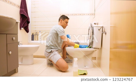 Man cleaning toilet in bathroom with disinfectant and sponge 123224767